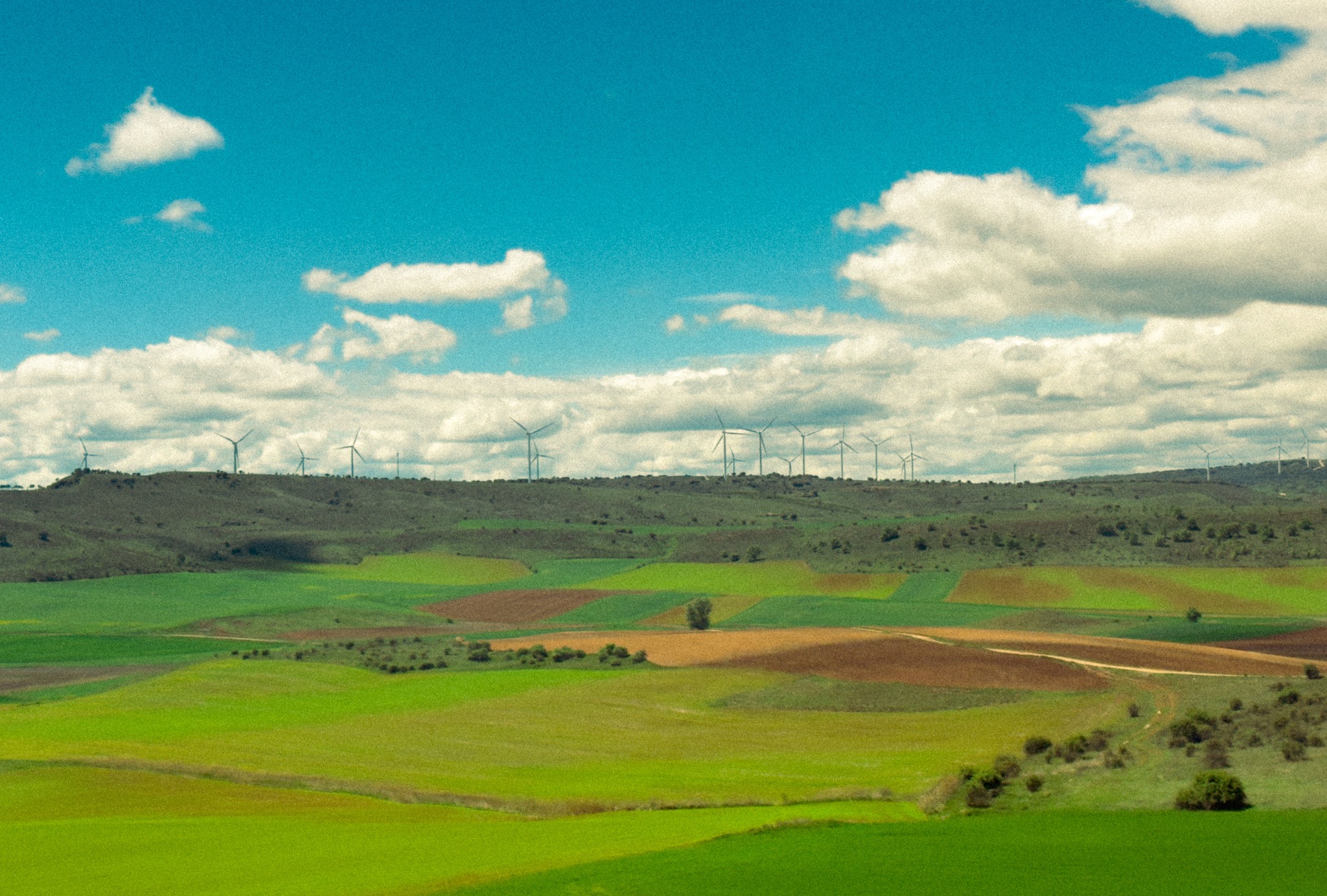Patchwork fields spread across a green Spanish valley beneath scattered clouds.